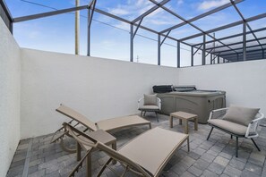 A covered outdoor patio with lounge chairs, a hot tub, and a grill.