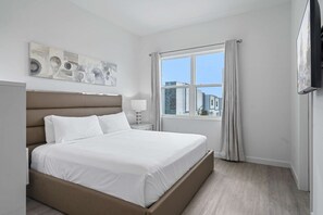 Et moderne hotelværelse med en stor seng, et vindue med gardiner, et fladskærms-tv og et billede på væggen.