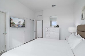 A hotel room with a large bed, a dresser, a mirror, and a television displaying a Disney theme.