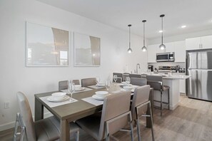 A modern kitchen with stainless steel appliances, a dining area with a table set for six, and pendant lighting.