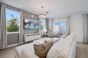 Una sala moderna con un televisor de pantalla plana grande, una araña y vistas de un parque infantil a través de la ventana.