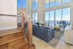 A spacious living area with a large window overlooking the ocean, a wooden staircase, and a seating area with a view.