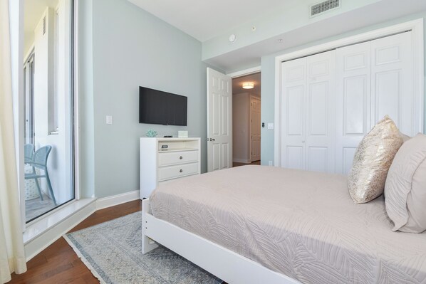 A bedroom with a bed, a TV mounted on the wall, a dresser, and a door leading to another room.