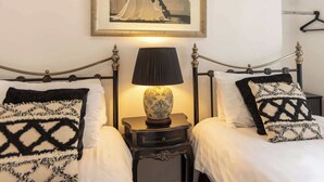 Una habitación de hotel con dos camas, cada una con un cojín estampado en blanco y negro, una mesita de noche con una lámpara y un cuadro en la pared.