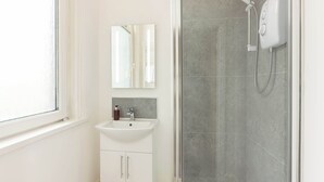 Un baño moderno con ducha envuelta en vidrio, un lavamanos blanco y un espejo encima.