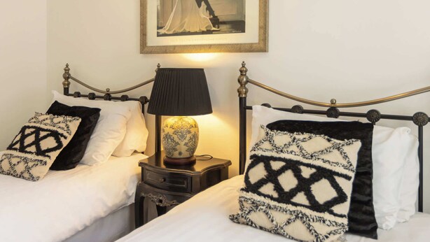 Una cama doble con almohadas estampadas en blanco y negro, una mesita de noche con lámpara, y un cuadro en la pared.