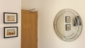 Un pasillo con una puerta de madera, dos cuadros en la pared y un espejo circular que contiene tres fotografías enmarcadas en su interior.