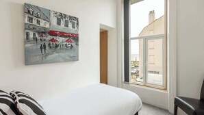 A bedroom with a bed, a chair, a window with a view of buildings, and a painting on the wall. - Host & Stay | Glaisdale at the Sandbeck (Whitby)