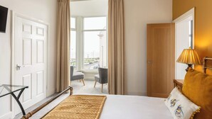 A hotel room with a bed, a desk, a chair, and a view of the street through large windows. - Host & Stay | Glaisdale at the Sandbeck (Whitby)