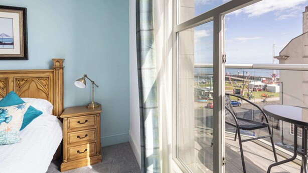 A bedroom with a bed, bedside table, lamp, and a view of a balcony with a table and chair. - Host & Stay | Grosmont at the Sandbeck (Whitby)