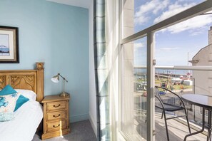 Un dormitorio con cama, mesita de noche, lámpara y vistas a un balcón con mesa y silla.