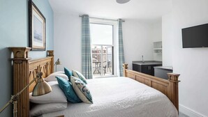 A bedroom with a large bed, a bedside lamp, a wooden headboard, a framed picture, and a view of a balcony with a table and chairs. - Host & Stay | Grosmont at the Sandbeck (Whitby)