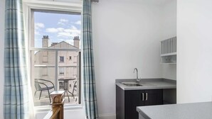 A compact kitchen with a window, a dining area with chairs, and a view of buildings outside. - Host & Stay | Grosmont at the Sandbeck (Whitby)