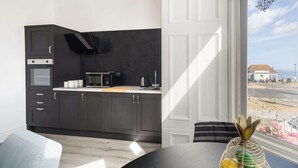 Une cuisine moderne avec des meubles de couleur sombre, un four à micro-ondes et une vue sur la mer par une fenêtre.