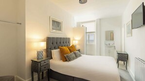 A bedroom with a large bed, two bedside tables, a nightstand, a mirror, and a television on the wall. - Host & Stay | Ruswarp Studio at the Sandbeck (Whitby)