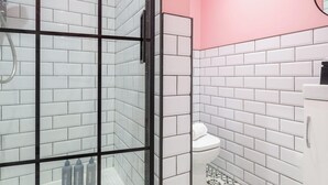 Un baño con azulejos blancos tipo metro, cabina de ducha de vidrio y una pared de acento rosa.