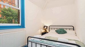 Un dormitorio pequeño y ordenado con una cama individual, una mesita de noche con lámpara y una ventana con cortinas azules.