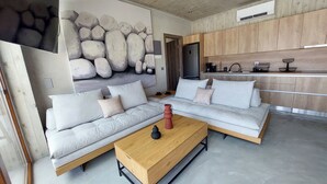 Ett modernt vardagsrum med en ljus soffa i sektionsmodell, ett soffbord i trä och en stor, abstrakt tavla på väggen.