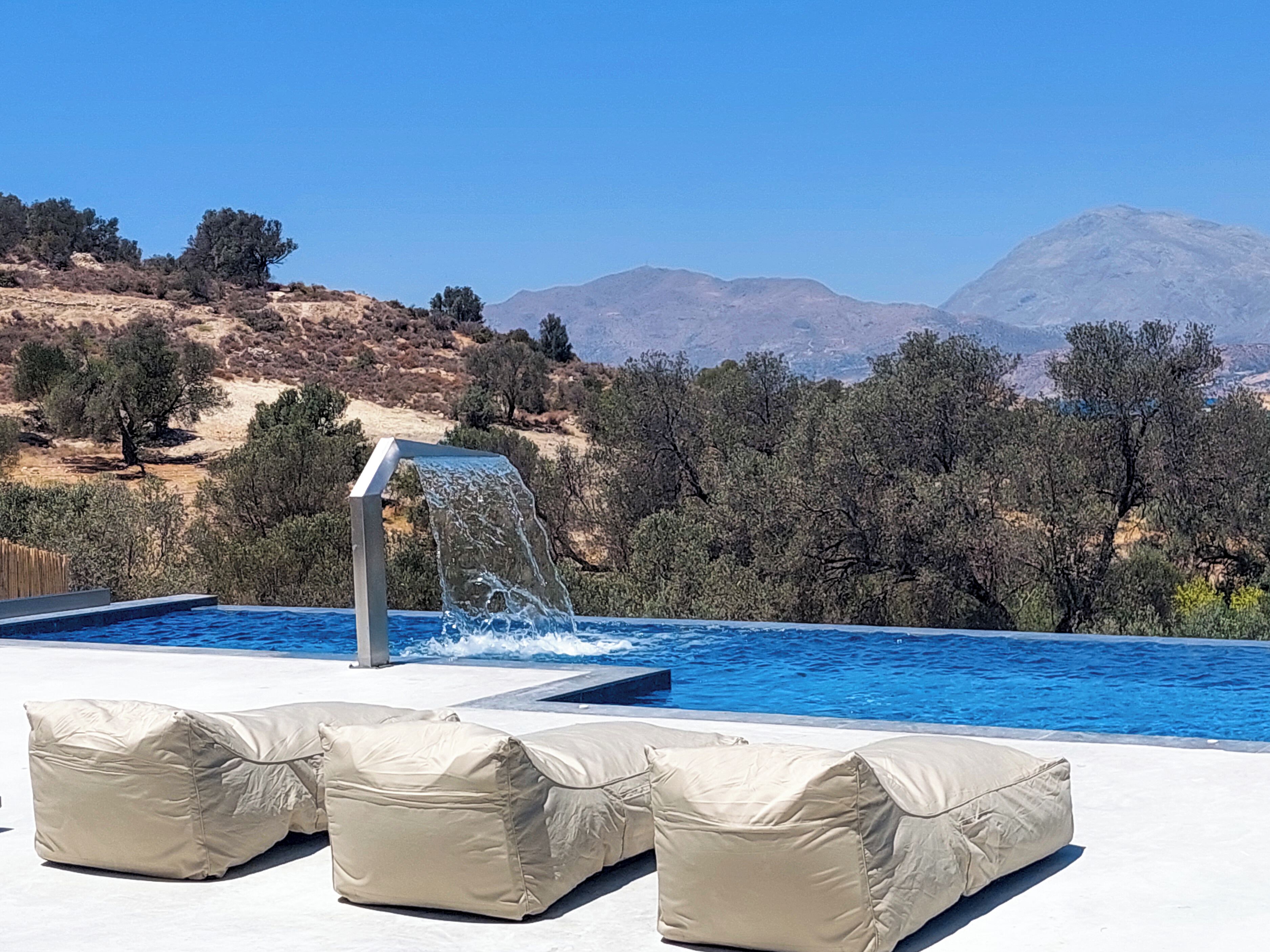 Une piscine agrémentée d’une cascade, entourée d’espaces de détente en plein air et dominée par un paysage montagneux.