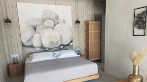 Ett modernt sovrum med en stor, abstrakt målning, en sängram i trä, sänglampor, en garderob i trä och ett litet bord med en vas.