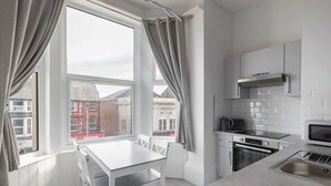 A modern kitchen with white cabinetry, a built-in oven, a microwave, and a window with curtains. - Host & Stay | Aberdeen Walk Apartment (Scarborough)