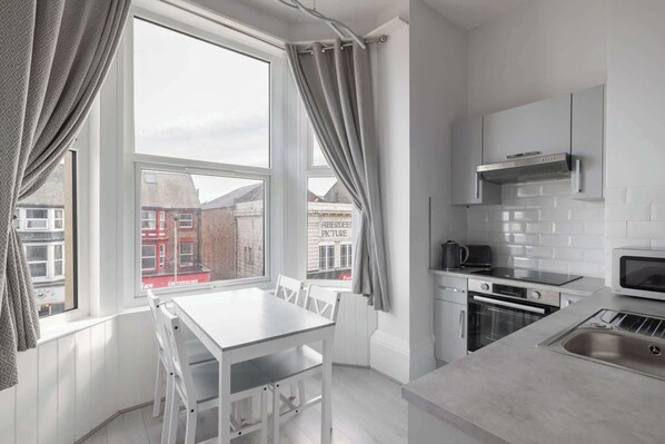 A modern kitchen with white cabinetry, a built-in oven, a microwave, and a window with curtains.