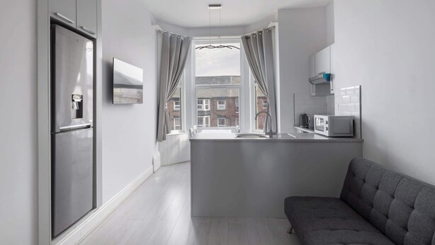 A modern kitchen with a built-in microwave, a grey sofa, and a window with curtains. - Host & Stay | Aberdeen Walk Apartment (Scarborough)