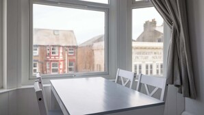 A room with a white table and chairs, large windows with a view of buildings, and a curtain on the right side. - Host & Stay | Aberdeen Walk Apartment (Scarborough)