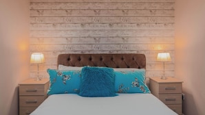 A bed with a tufted headboard, two bedside tables with lamps, and a wall with repeated text and heart motifs.