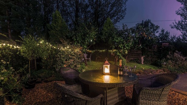 An outdoor dining area with wicker chairs and a round table, surrounded by trees and string lights.