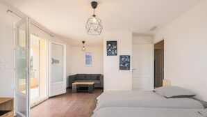 A modern bedroom with a large bed, a sofa, and a dining table. There is a sliding glass door leading to a balcony. - Spacious, quiet Villa Niçoise with swimming pool (Nice)