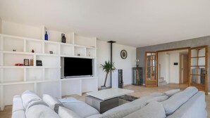 A modern living room with a grey sofa, a flat-screen TV, white shelving, and a potted plant. - Spacious, quiet Villa Niçoise with swimming pool (Nice)