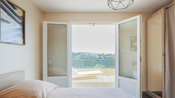 A hotel room with a bed, a view of the city through a glass door, and a balcony with a chair. - Spacious, quiet Villa Niçoise with swimming pool (Nice)