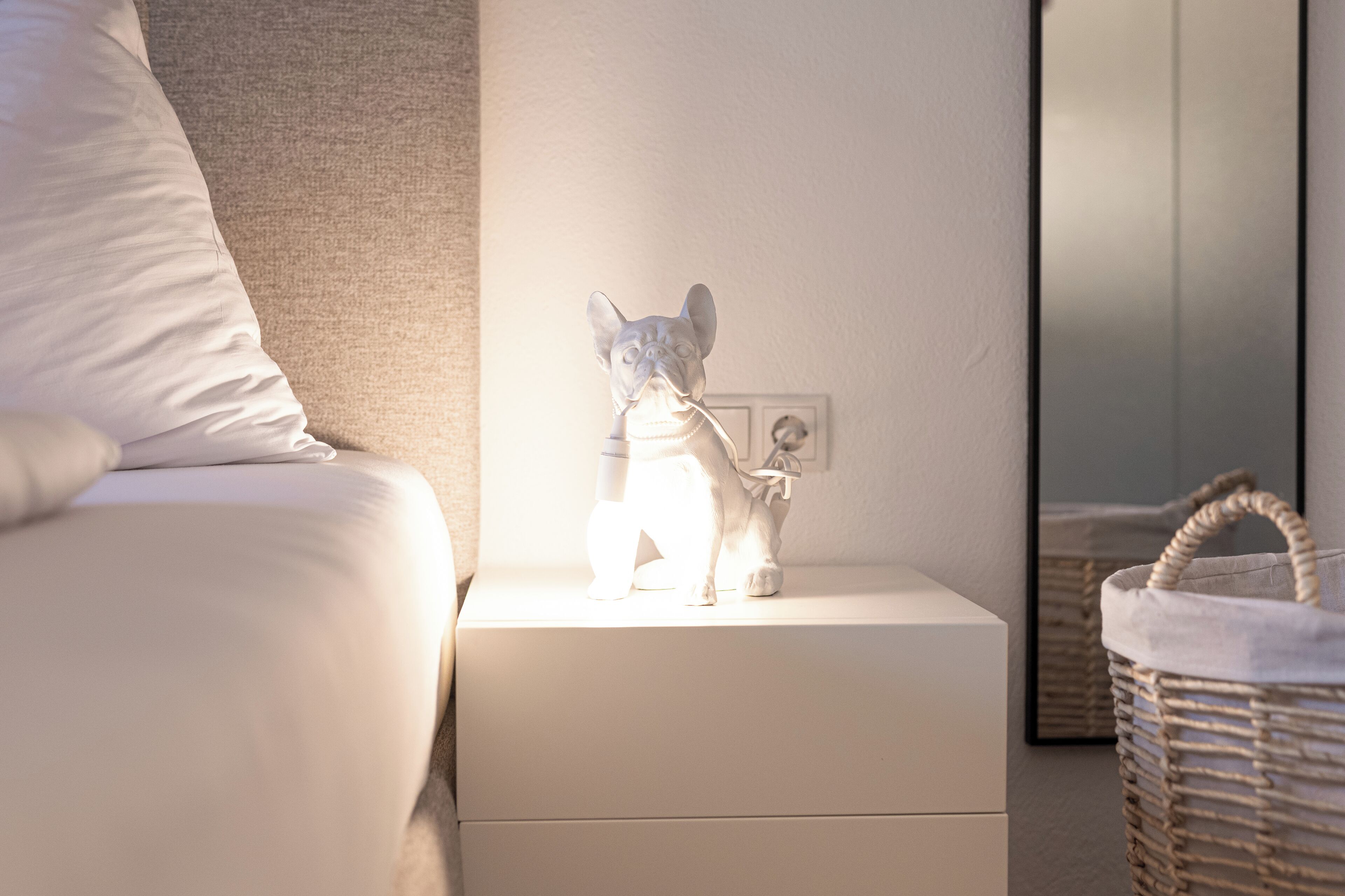 A white bedside table with a small dog figurine and a basket.