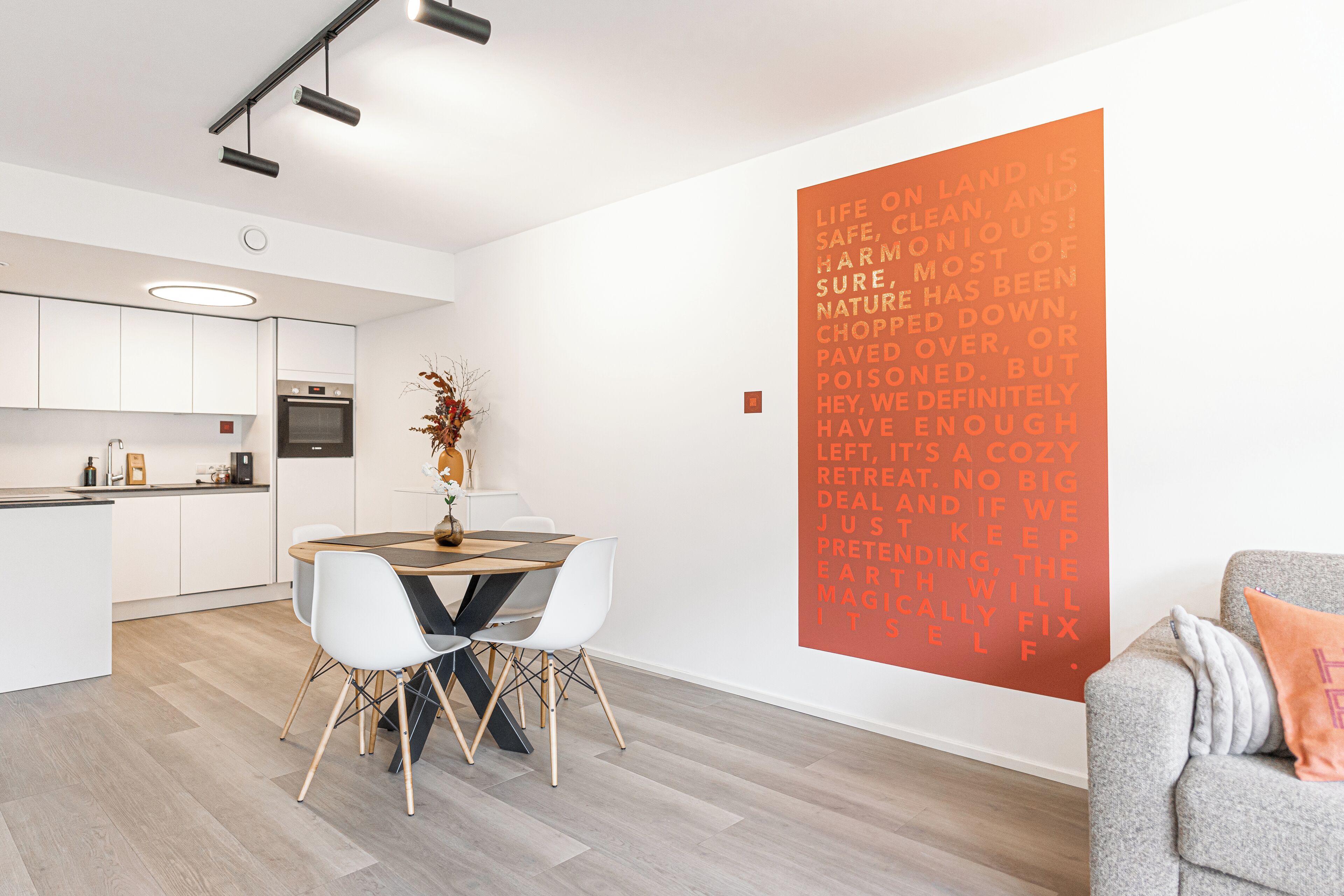 A modern kitchen with white cabinets, a built-in oven, and a dining area with a wooden table and white chairs.