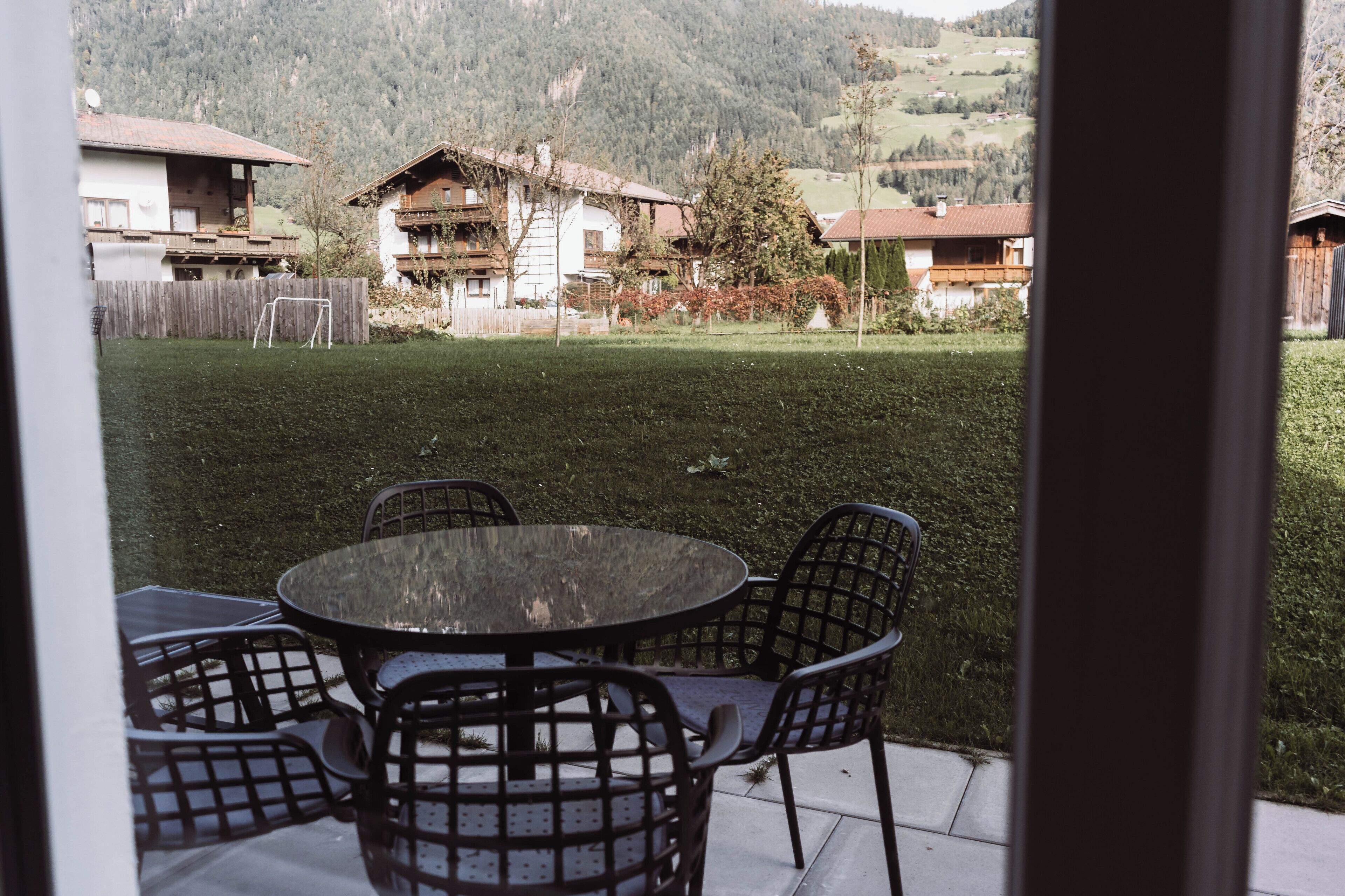 Une terrasse avec une table ronde et des chaises, une vue sur un paysage montagneux et une clôture en bois en arrière-plan.