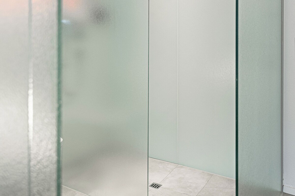 A glass-enclosed shower with a tiled floor and a visible drain.