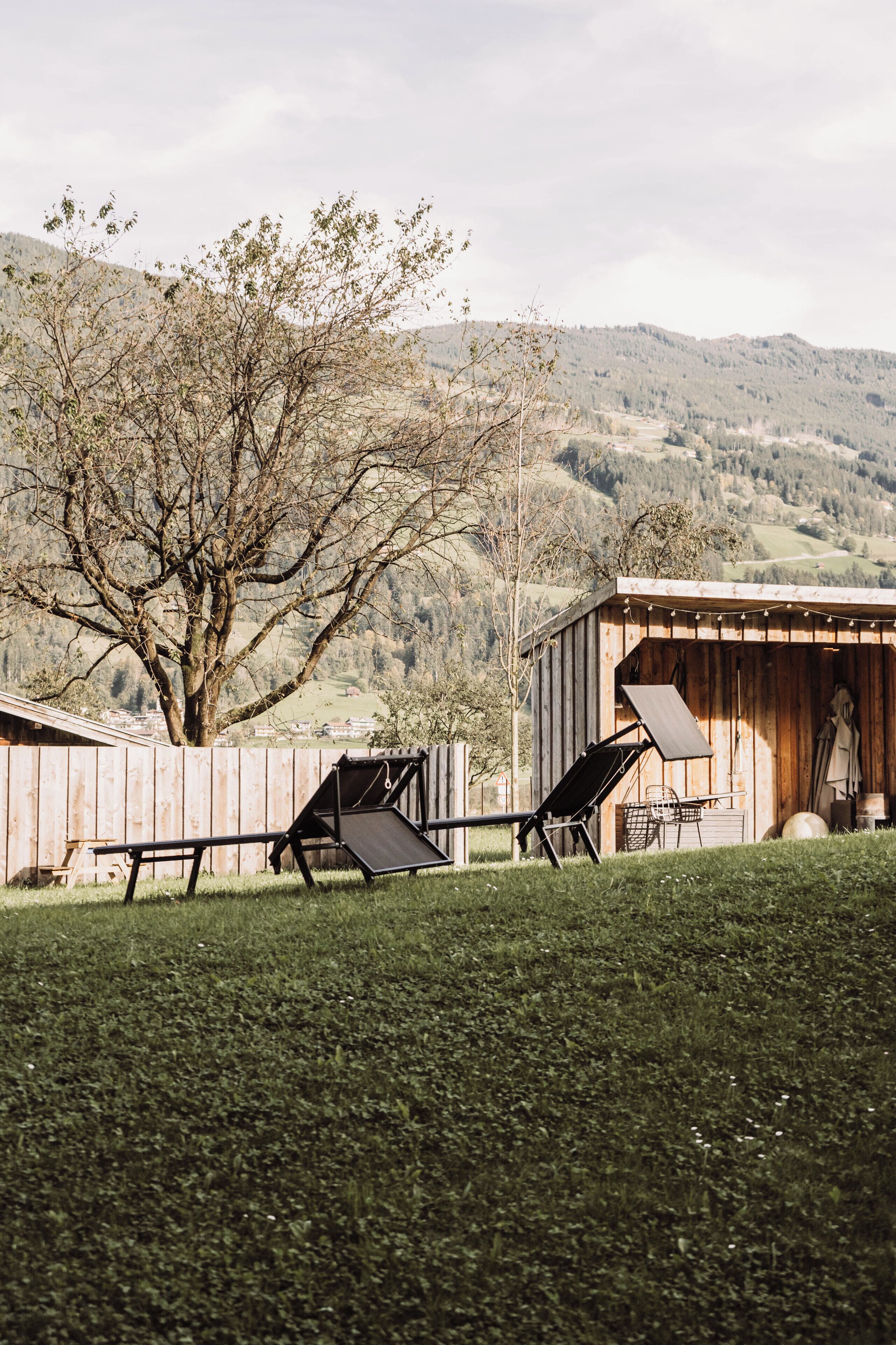 A rustic wooden shed with a slanted roof, a metal chair, and a table outside.