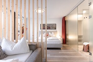 Habitación de hotel moderna con una cama, un sofá, una separadora de madera y una puerta de cristal.