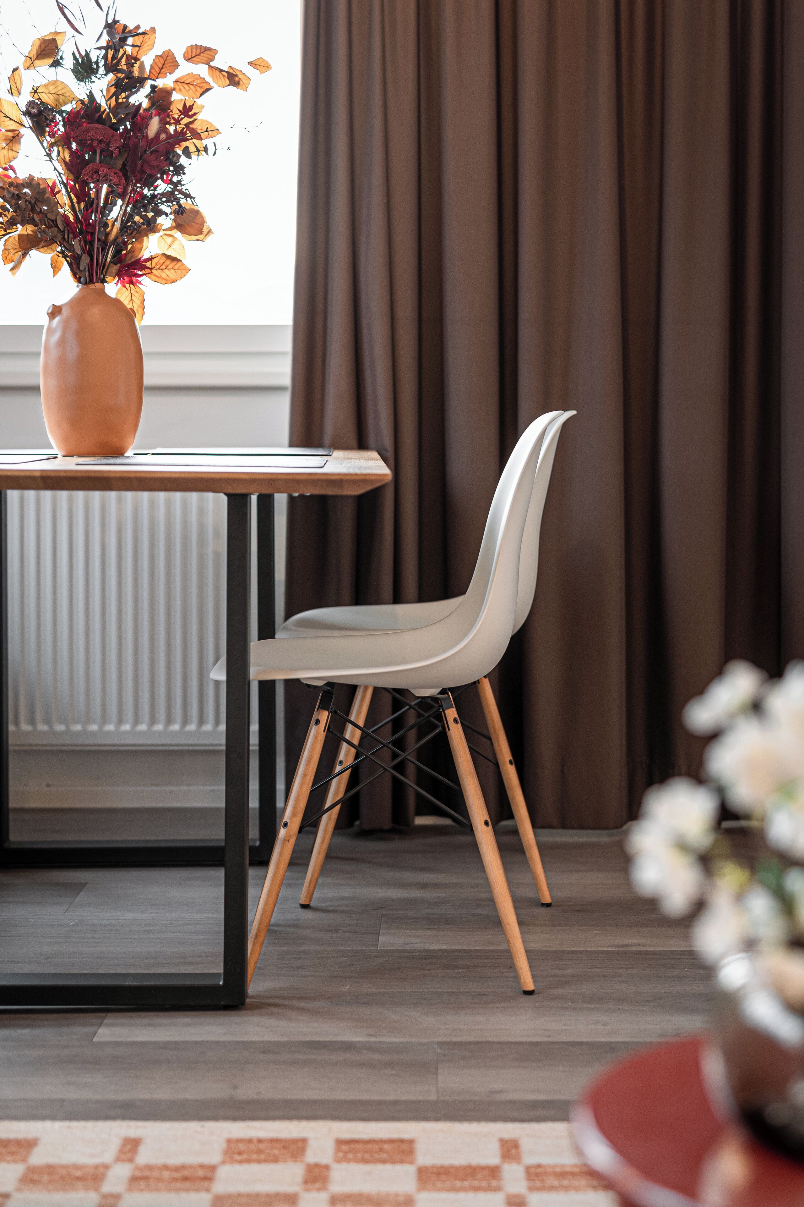 A modern dining area with a table, a white chair, and a vase of flowers.
