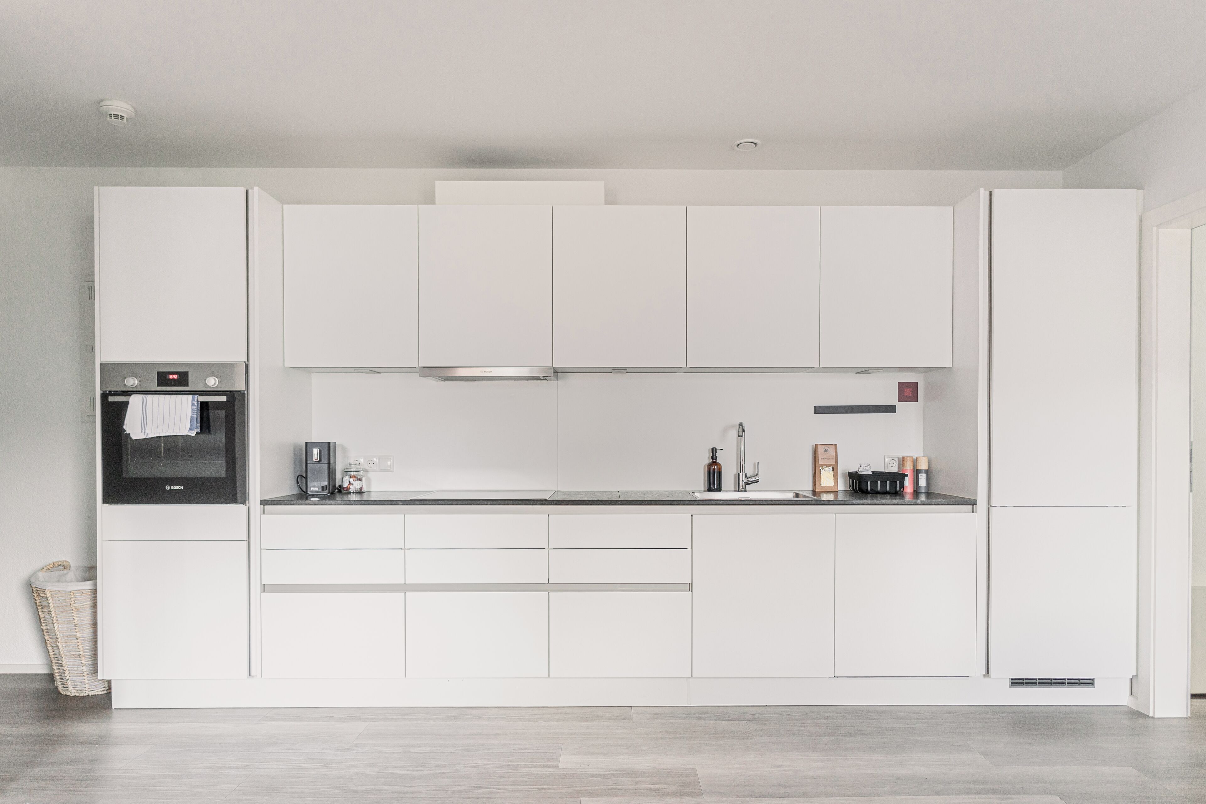 Eine moderne Küche mit weißen Schränken, einem eingebauten Backofen und einer Edelstahl-Dunstabzugshaube.