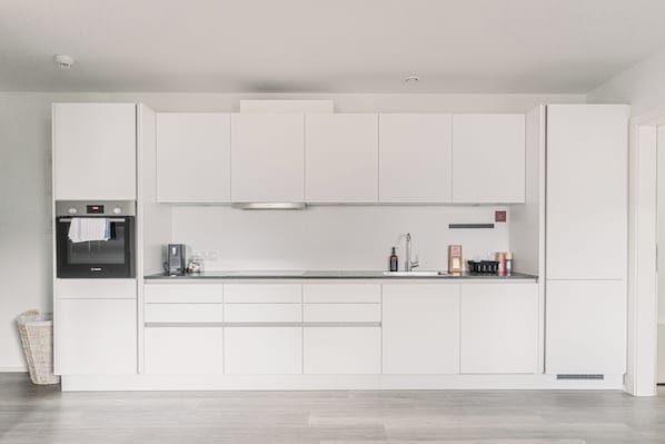 A modern kitchen with white cabinets, a built-in oven, and a stainless steel range hood. - Lebe'schlitters - Im Zillertal (Schlitters)
