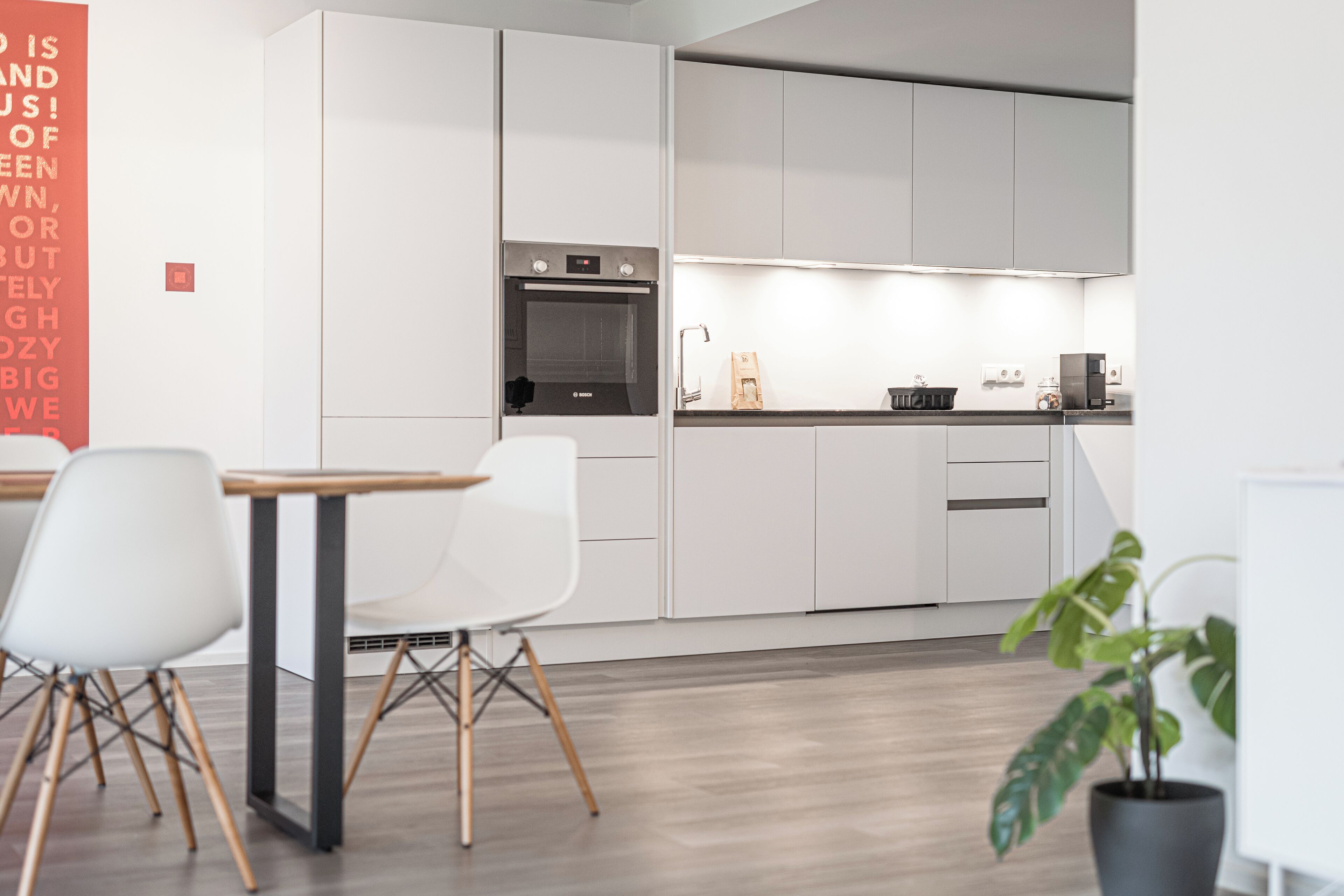 A modern kitchen with white cabinetry, a built-in oven, and a dining area with a table and chairs.