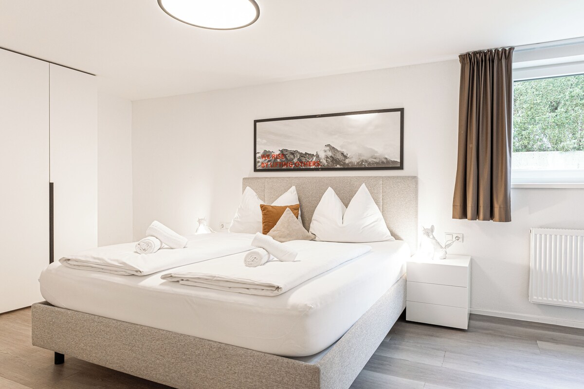 A modern bedroom with a large bed, a bedside table, a framed picture, and a window with curtains.