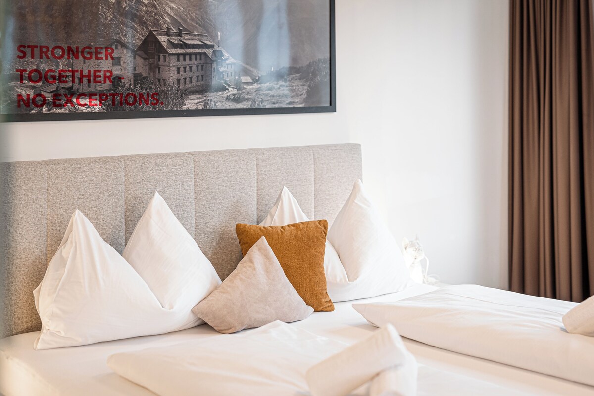 A hotel room with a bed, pillows, and a framed picture on the wall.