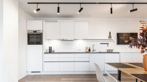 A modern kitchen with white cabinetry, a built-in oven, and a dining area with a wooden table and chairs. - Lebe'schlitters - Im Zillertal (Schlitters)