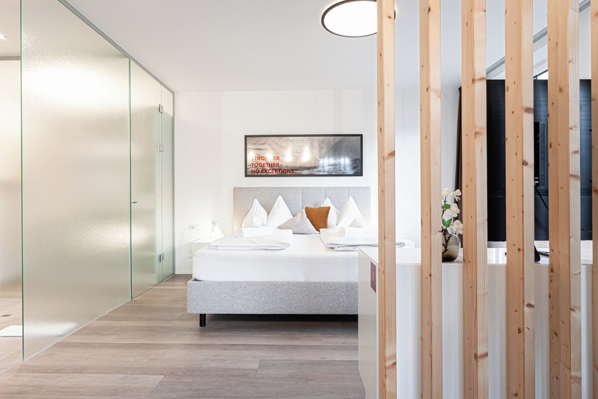 A modern hotel room with a bed, a large window, and a wall-mounted artwork.