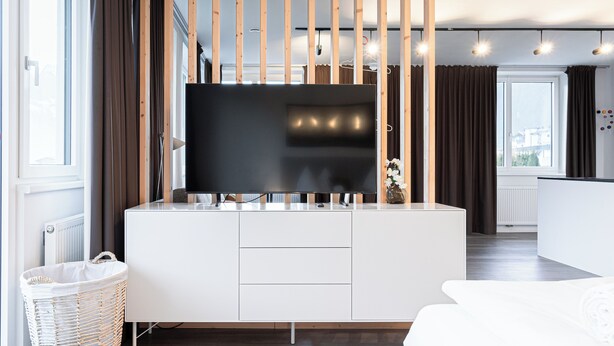 A modern kitchen with a large flat-screen TV, white cabinetry, and a wicker basket. - Lebe'schlitters - Im Zillertal (Schlitters)