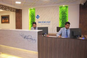 A reception desk at Shada Pathor Sylhet Hotel & Resort with two staff members.