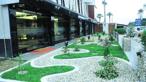 A modern building with a glass facade, landscaped garden with green grass and white pebbles, and a red carpet leading to the entrance. - Shada Pathor Hotel & Resort Sylhet  (Companiganj)